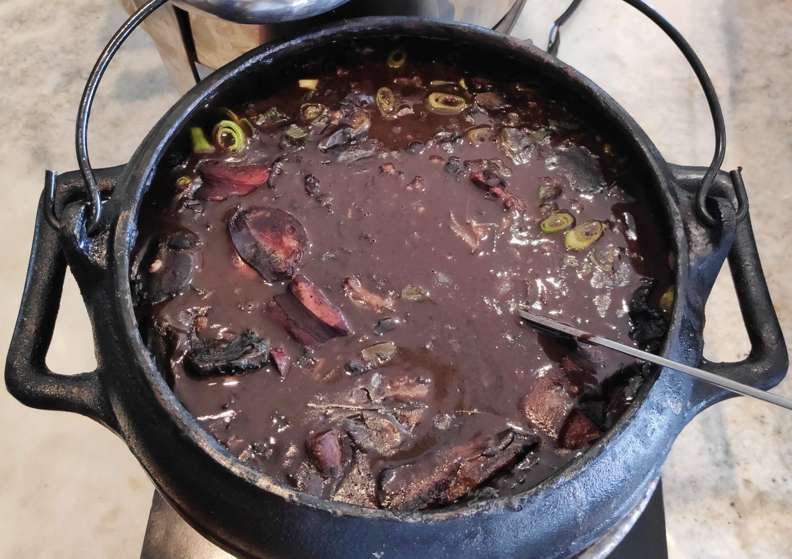 A black clay pot of feijoada with black beans, pork and sausage