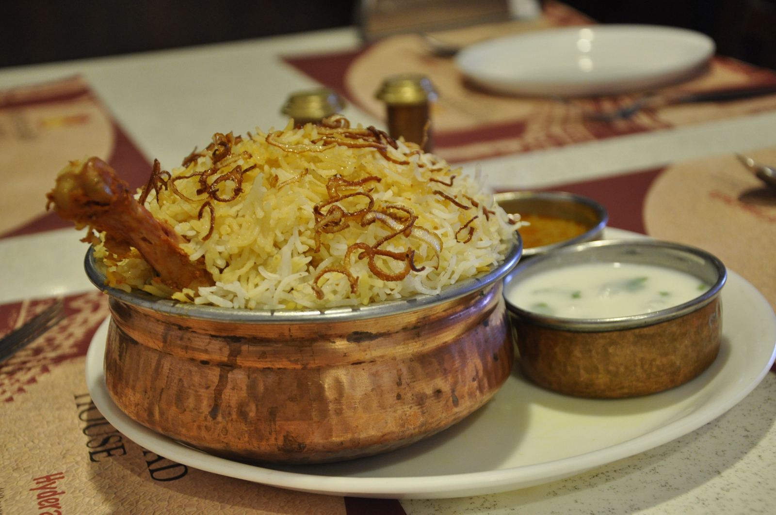 Chicken biryani with saffron-tinted rice and fried onions in a copper bowl with raita