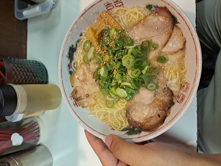 A bowl of ramen with sliced pork, green onions and wavy noodles in broth