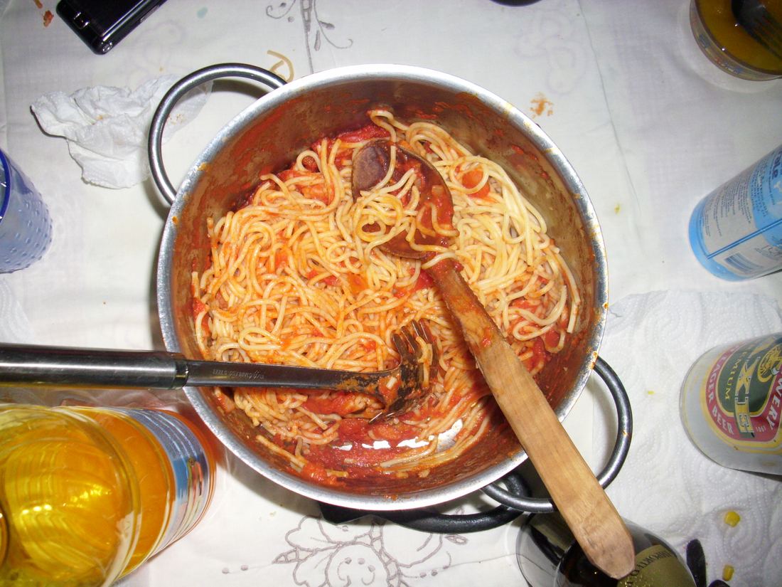 A pan of spaghetti tossed in tomato sauce with a wooden spoon