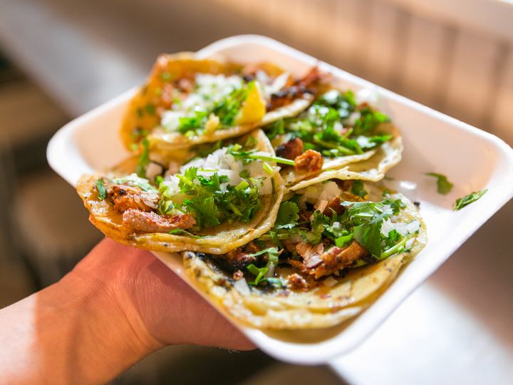 Hand holding a tray of al pastor tacos with onion and cilantro