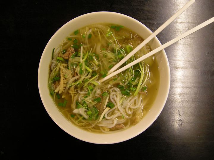 A bowl of pho with rice noodles, herbs and chopsticks on a dark table